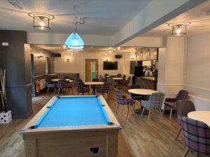 picture of club's lounge with blue pool table, wood effect flooring, white tables and mixed seating