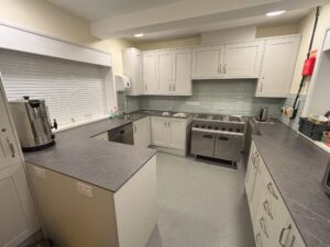 Picture of kitchen showing grey cabinets, dishwasher, and cooker with 6 hobs